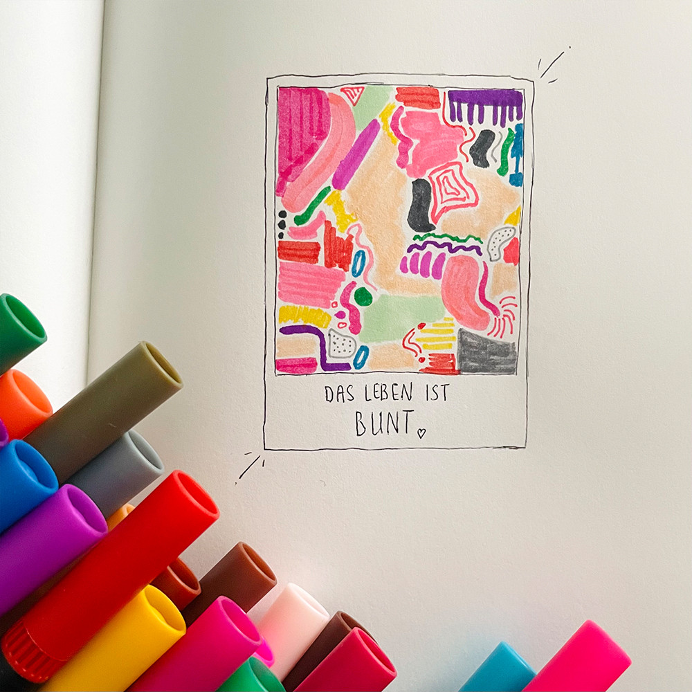 Einblick in ein Skizzenbuch mit einer sehr bunten Skizze, daneben eine Palette voller Stifte